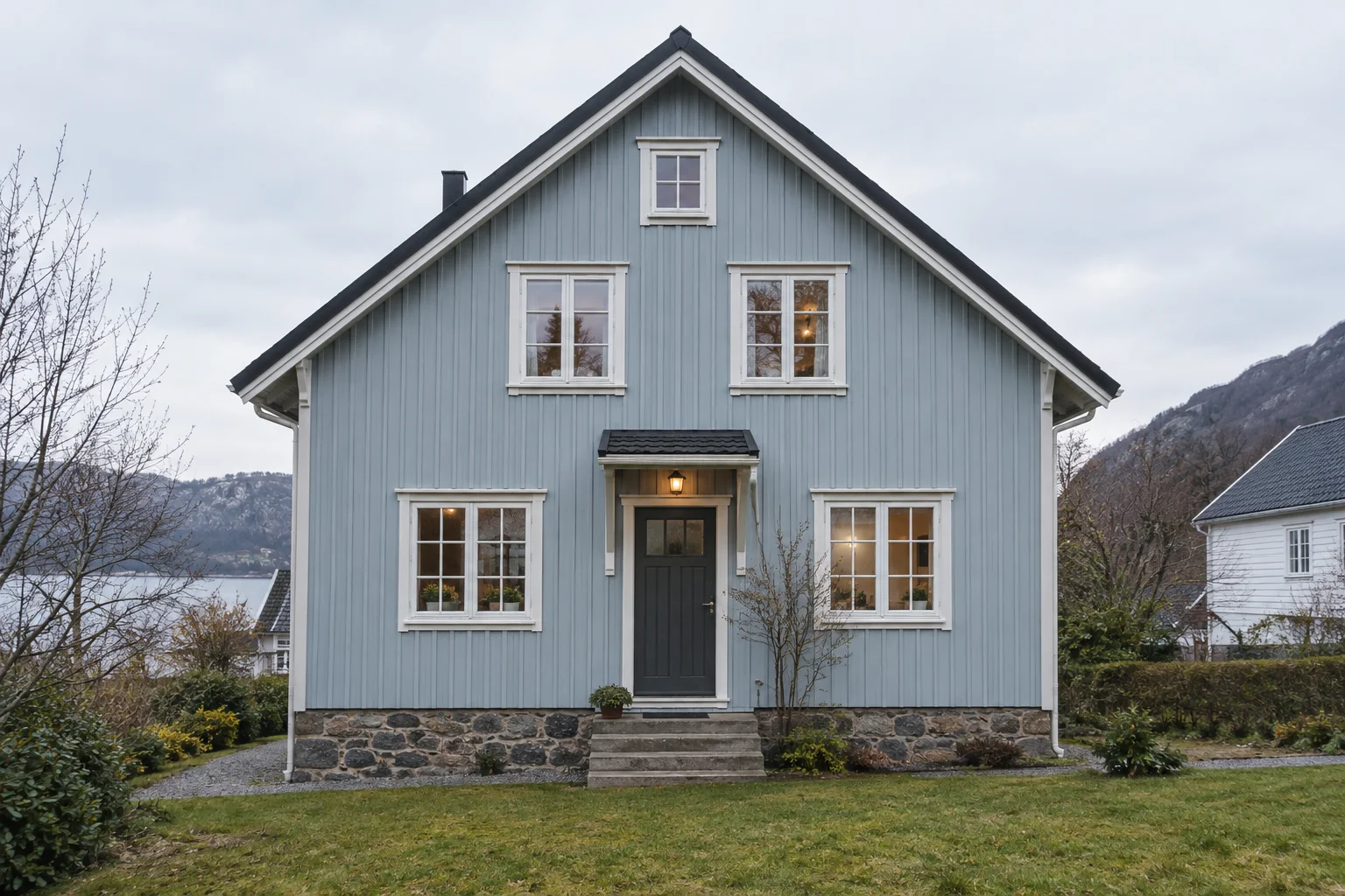 Gavlfasaden på et blågrått trehus med tydelige vinduer, dør, sokkel og takkanter.
