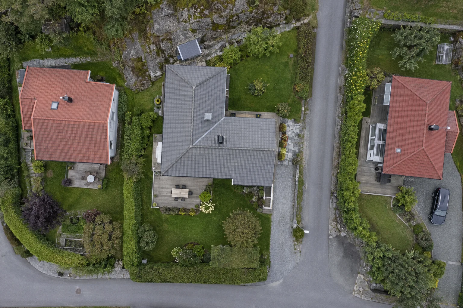 Tre hustak, hager og en smal vei sett rett ovenfra.