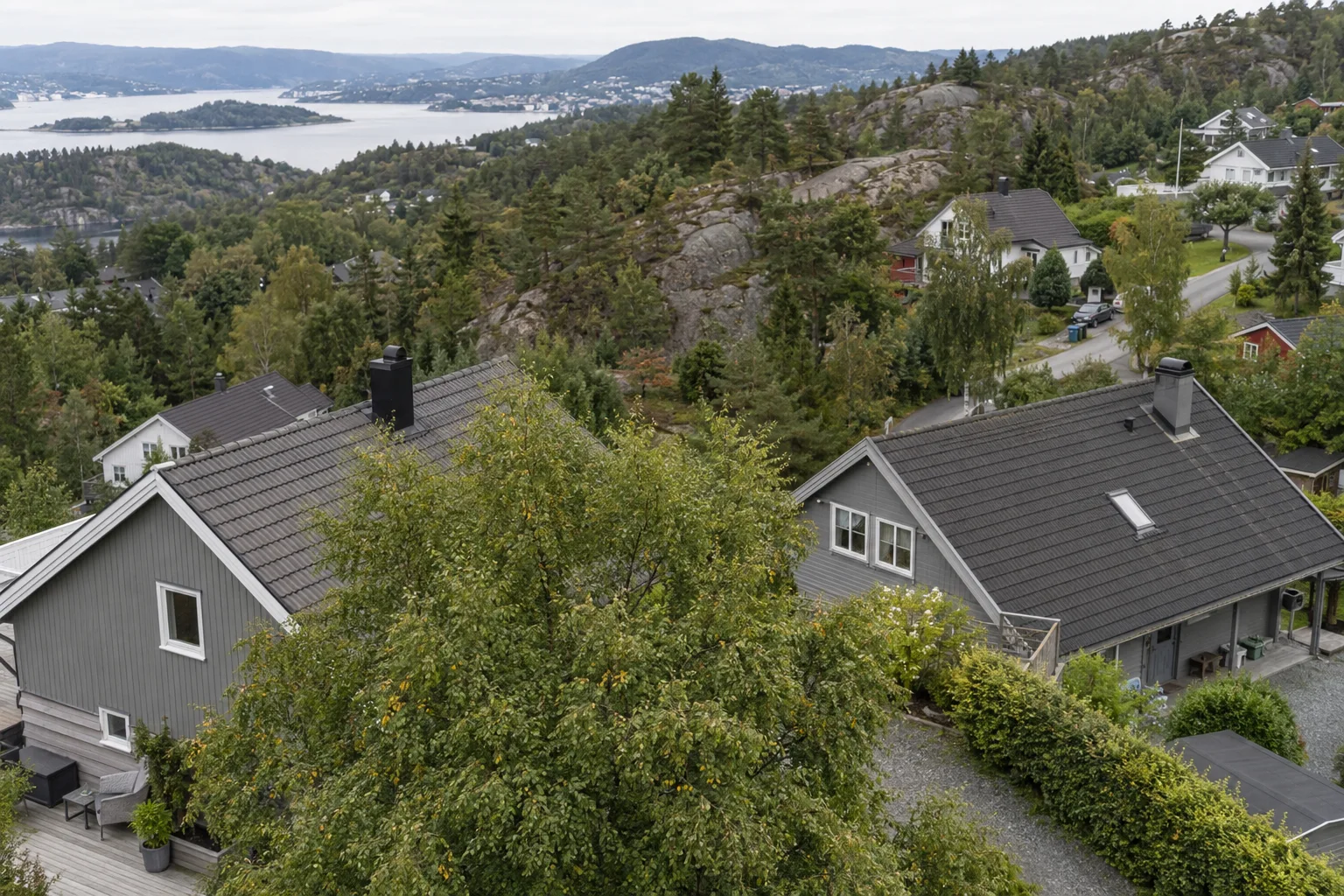Hustak i skrånende terreng, med et tre som skjuler en del av taket.