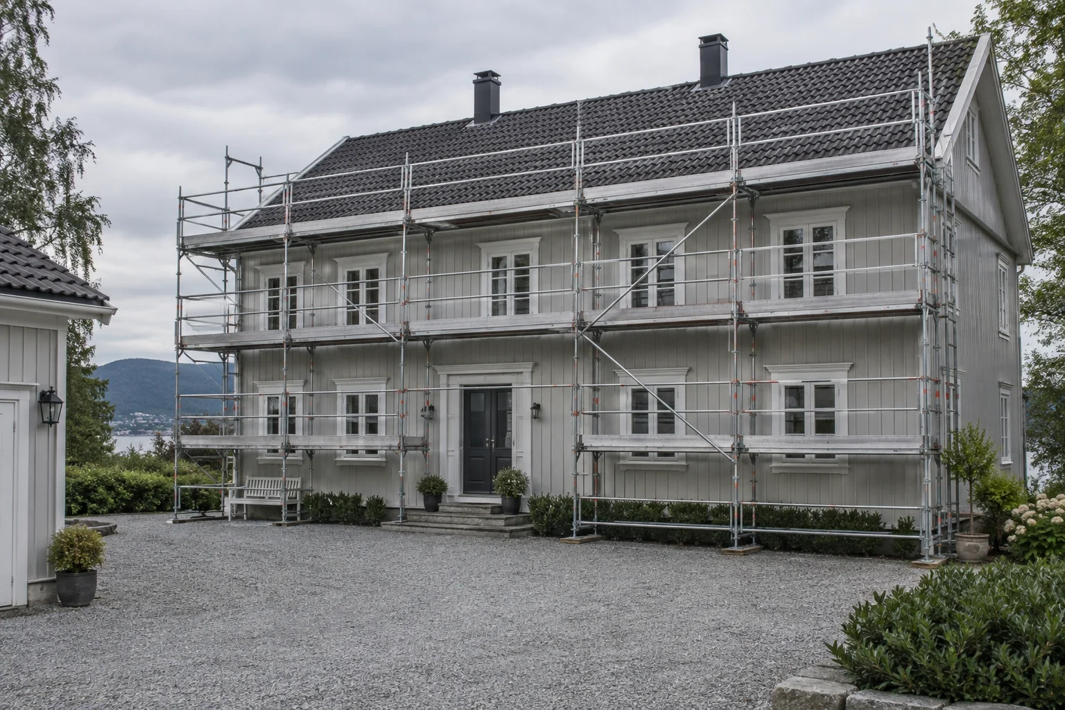 Et grått trehus med fasadestillas langs den synlige langveggen.