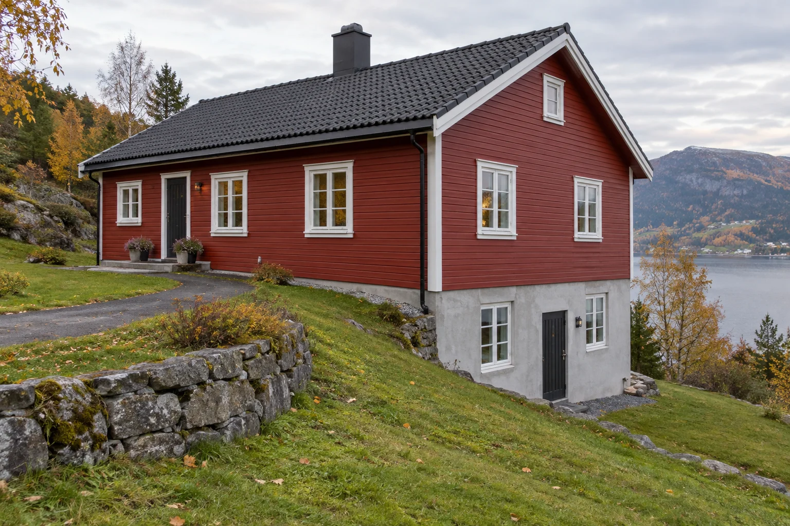 Rødt trehus i en skråning med mer synlig grunnmur på nedsiden.